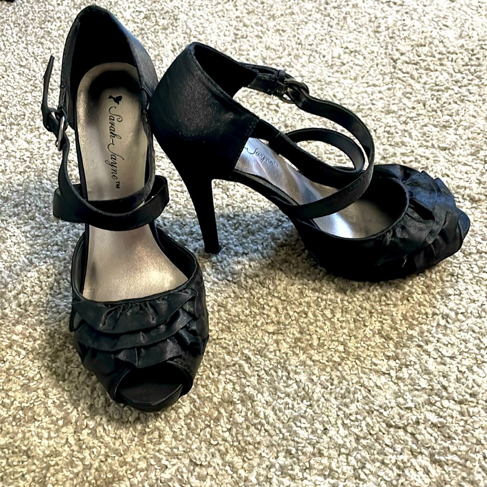 Black satin heels with ruffle details and crossed straps.